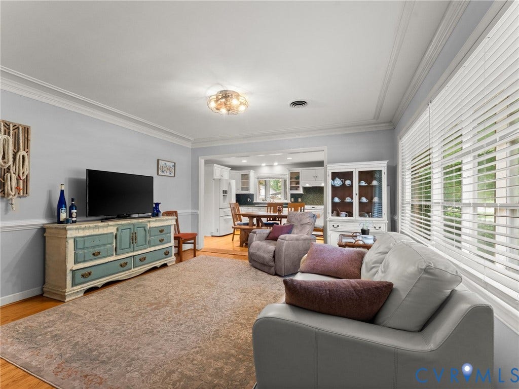 Living area featuring wood-finish flooring, crown molding, a decorative ceiling light fixture, and an entry to an additional room