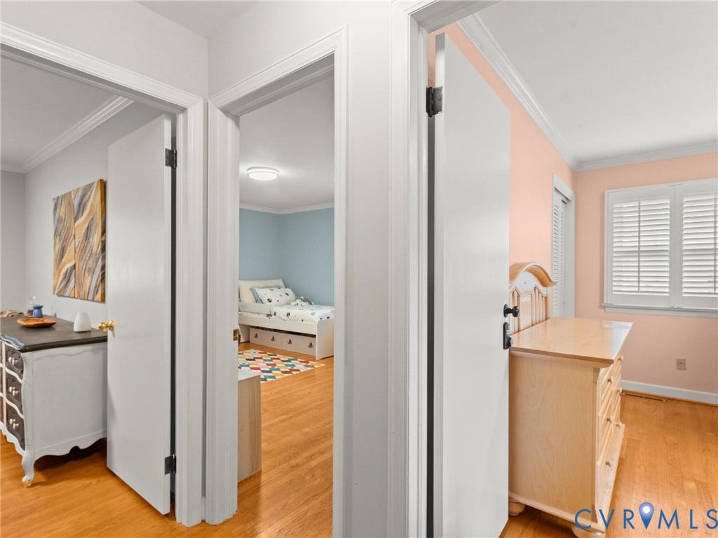 Hallway featuring wood-finish flooring, white doors with dark hardware, and crown molding