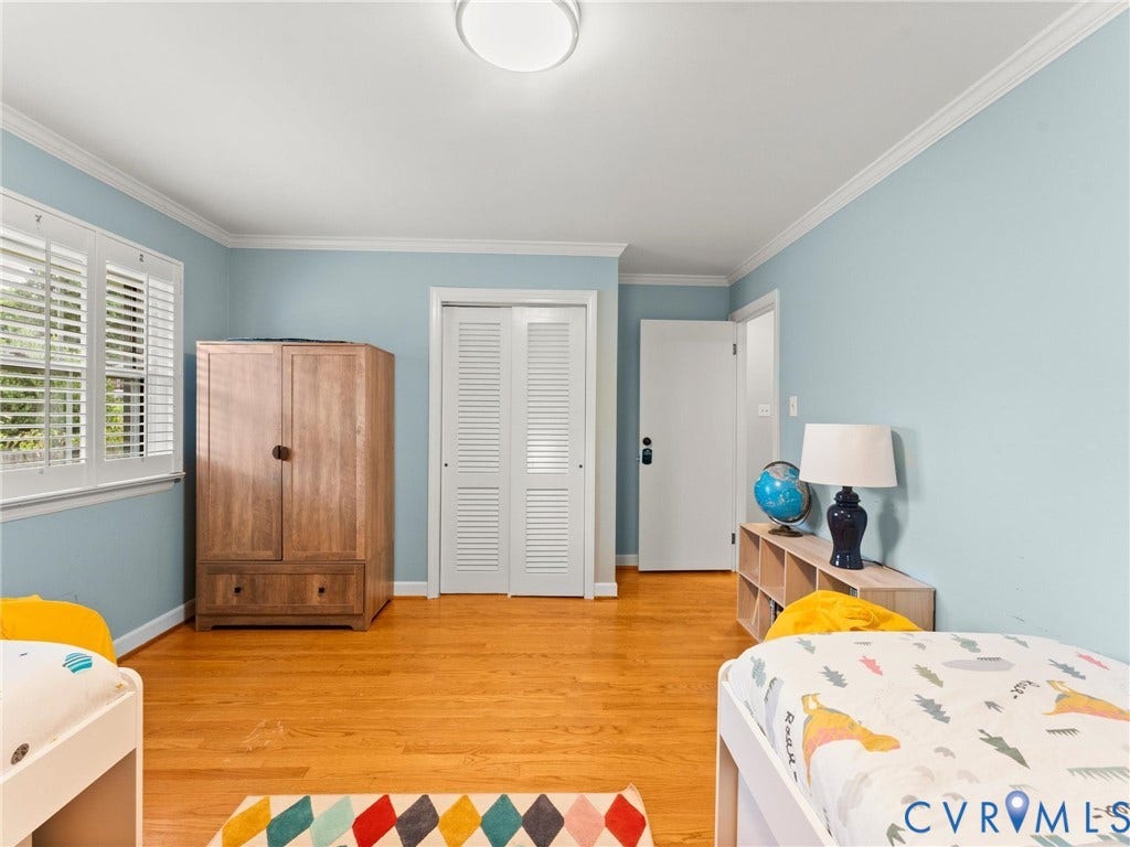 Spacious bedroom featuring light blue walls, wood-finish flooring, and abundant natural light from shuttered windows