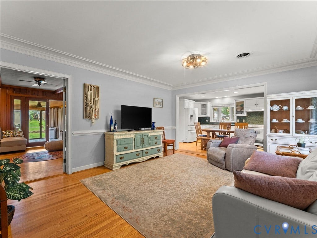 Hardwood flooring throughout the living area, featuring crown molding, an integrated kitchen space with white cabinetry, and a sunroom with outdoor access