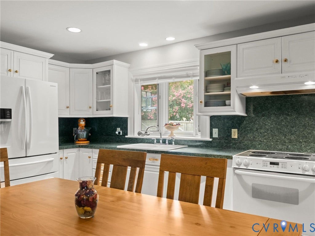 Bright, chef-inspired kitchen featuring crisp white cabinetry with glass-front upper cabinets and brass hardware, deep forest green tile backsplash, white subway tile accents, and stainless steel appliances including a slide-in range and refrigerator