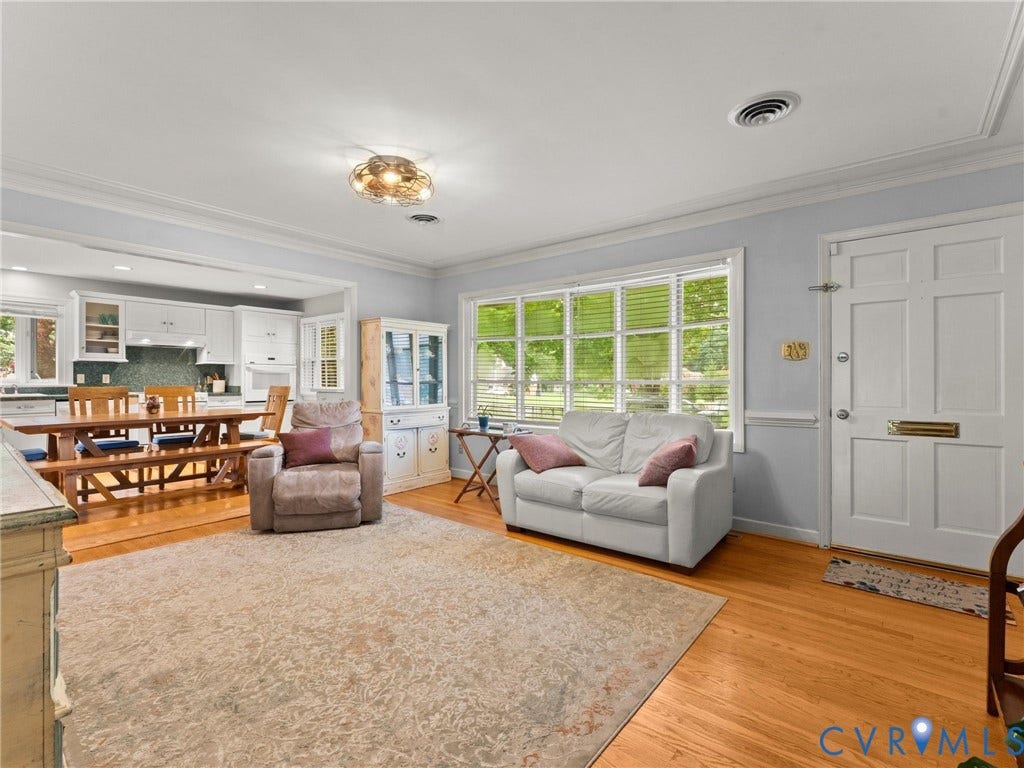 Bright living area featuring wood-finish flooring and a front entry door with a brass mail slot