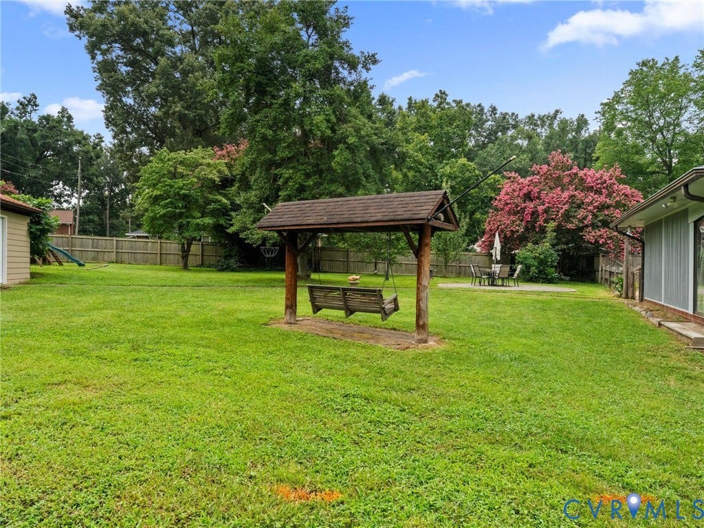 Expansive backyard featuring a covered porch swing, privacy fencing, mature trees, a concrete patio, and a screen-enclosed area