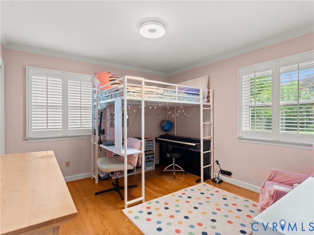 Bright, versatile bedroom featuring hardwood flooring, plantation shutters on dual windows, and abundant natural light