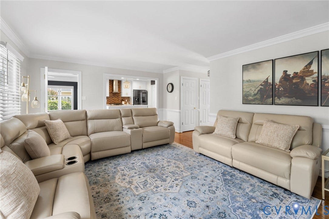 Sophisticated living room showcasing dual cream leather sectionals with power recline functionality, hardwood flooring, and abundant natural light from multiple windows