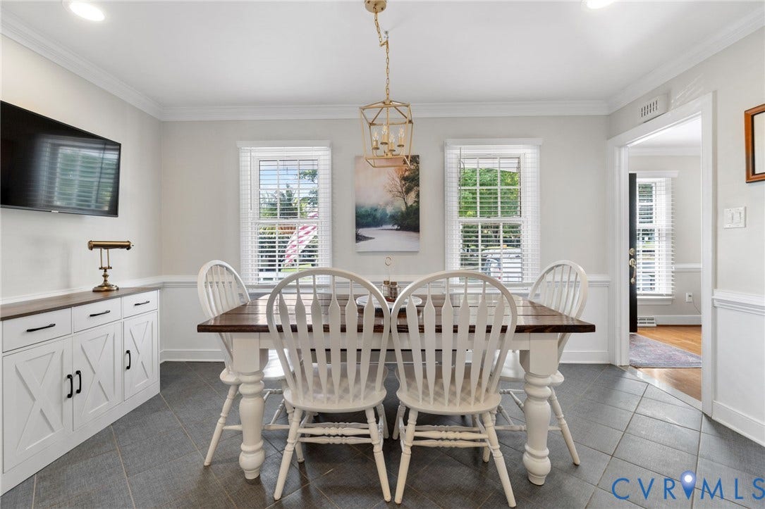 Bright dining room showcasing a wood-finish table with turned spindle-back chairs, slate-finish tile flooring, and abundant natural light from three multi-pane French doors with plantation shutters
