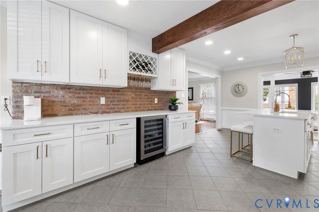White shaker cabinetry, brick-finish backsplash, built-in wine storage, stone countertops, and tile flooring
