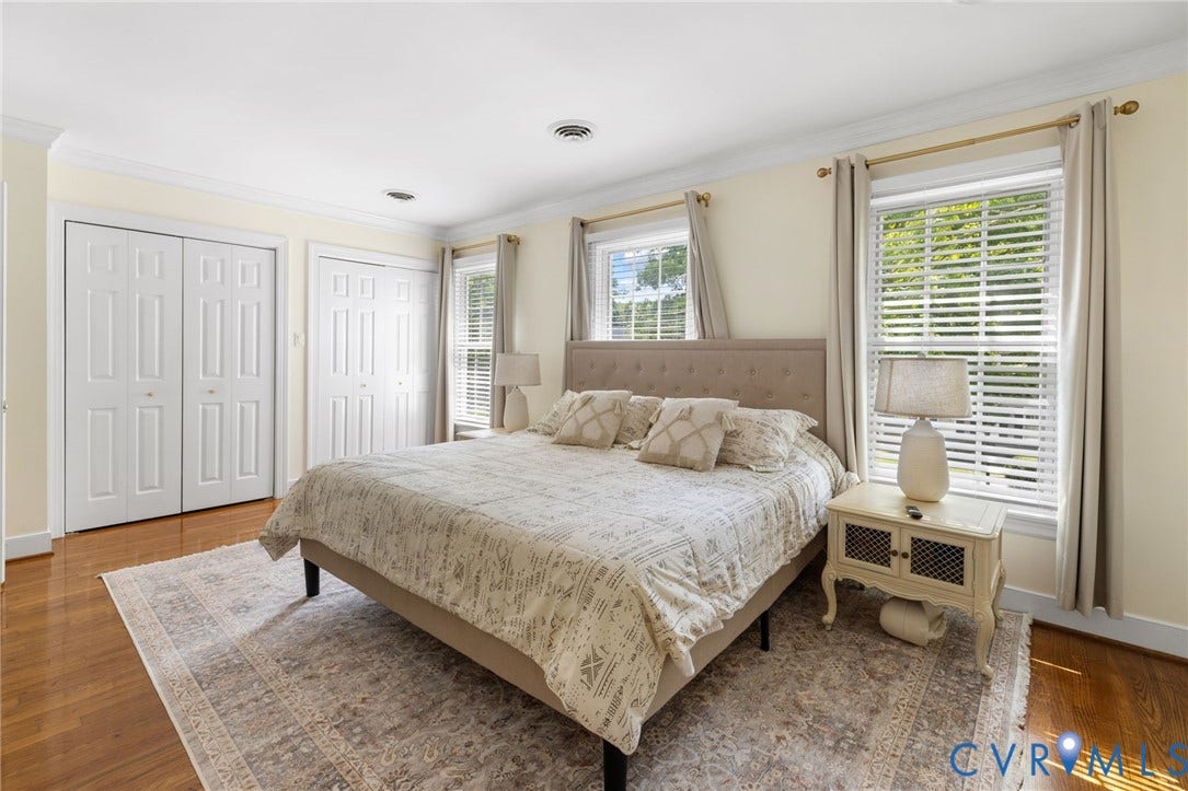 Spacious primary bedroom showcasing hardwood flooring, a neutral color palette, and abundant natural light from multiple windows with plantation shutters