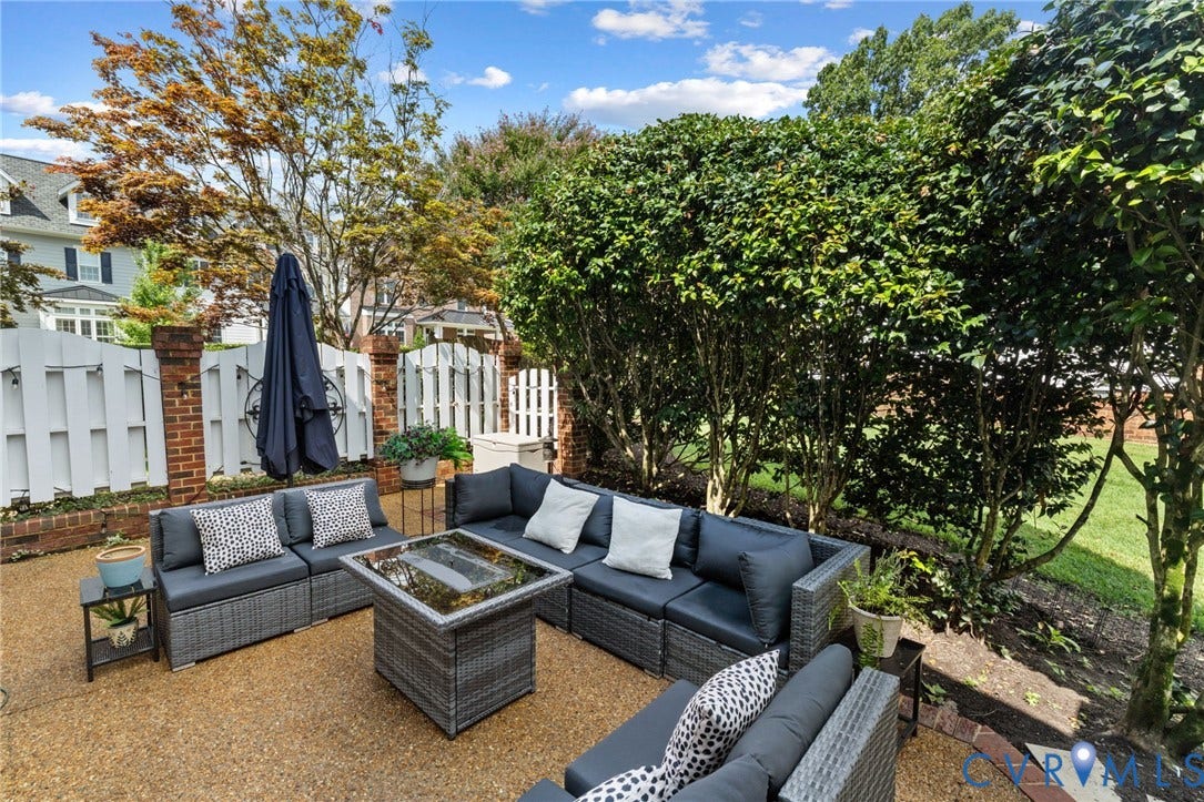 Expansive patio with aggregate surfacing, bordered by mature privacy plantings and a decorative white fence with brick pillars
