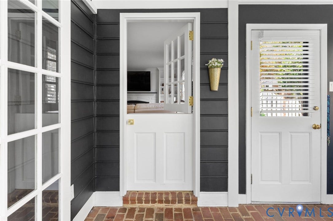 Welcoming entryway featuring white Dutch-door with brass hardware, dark horizontal shiplap walls, brick flooring, and sidelights with functional shutters