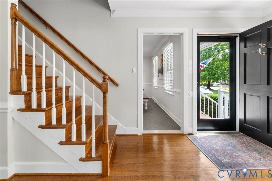 Hardwood flooring, wood staircase with white balusters, paneled front door, white trim, and a transom window