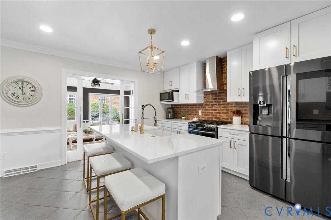 Kitchen featuring a central island with countertop seating, white cabinetry, integrated stainless-steel appliances, and a brick-finish backsplash