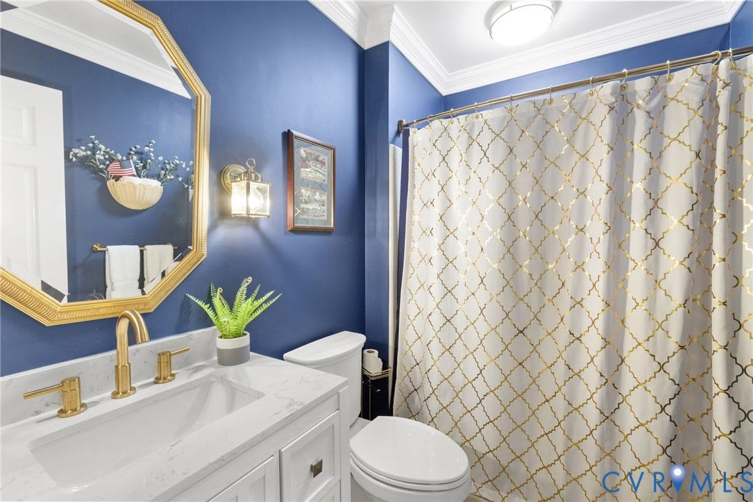 Vanity with integrated sink and gold-tone faucet, octagonal mirror with gold-tone frame, wall-mounted light fixture, and crown molding