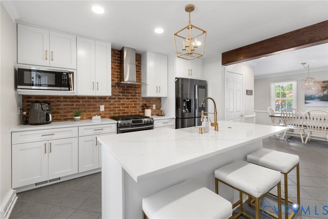 White shaker cabinetry, brick-style backsplash, stainless steel range with hood, black French door refrigerator, and a kitchen island with a gold-finish faucet