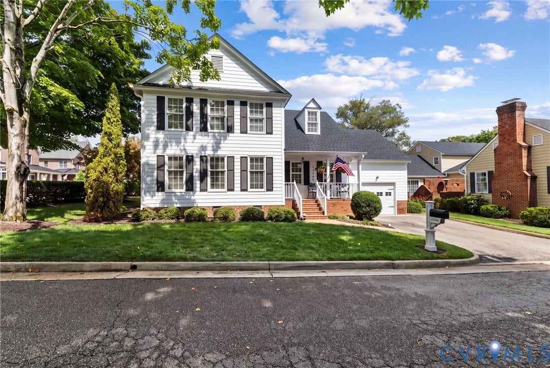 Classic Colonial-style residence featuring a two-story white exterior with black shutters, multiple double-hung windows, and brick chimney detailing
