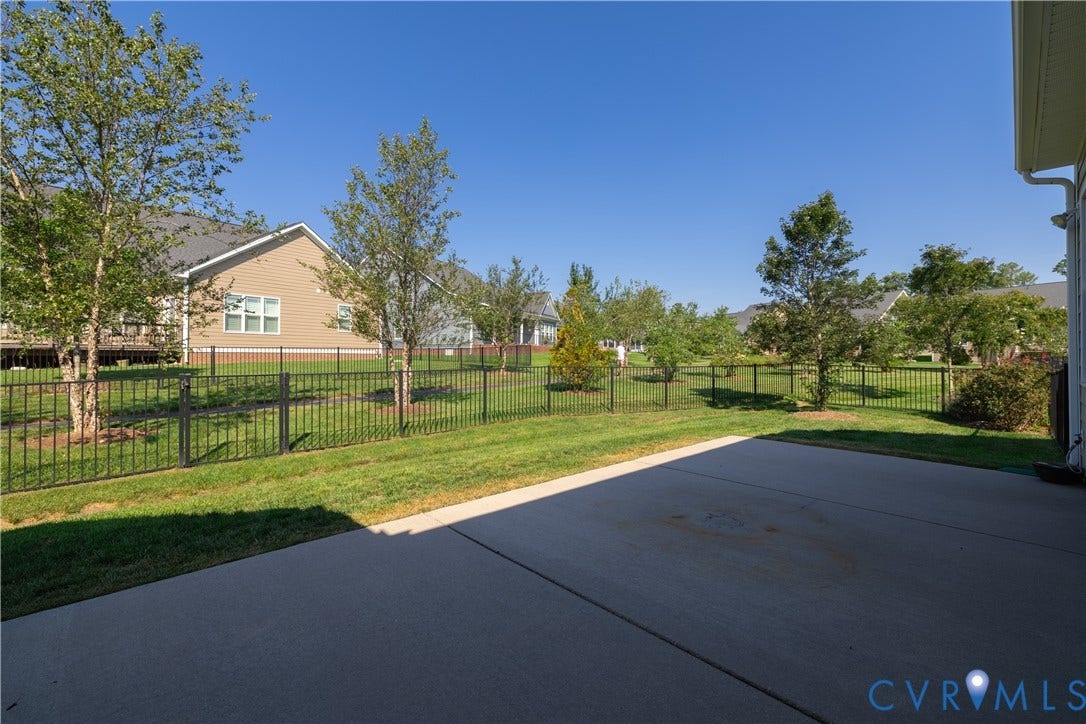 Expansive backyard featuring a concrete patio, manicured lawn, and black metal fencing