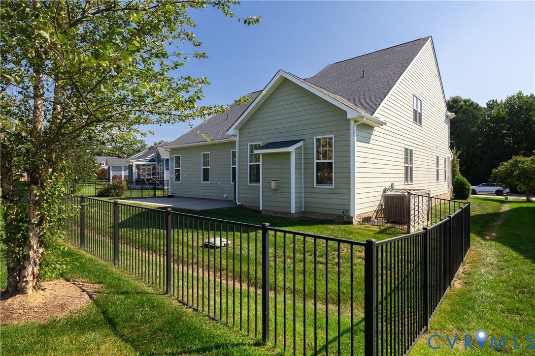 Expansive backyard featuring a manicured lawn, established tree, black metal fencing, and a concrete patio