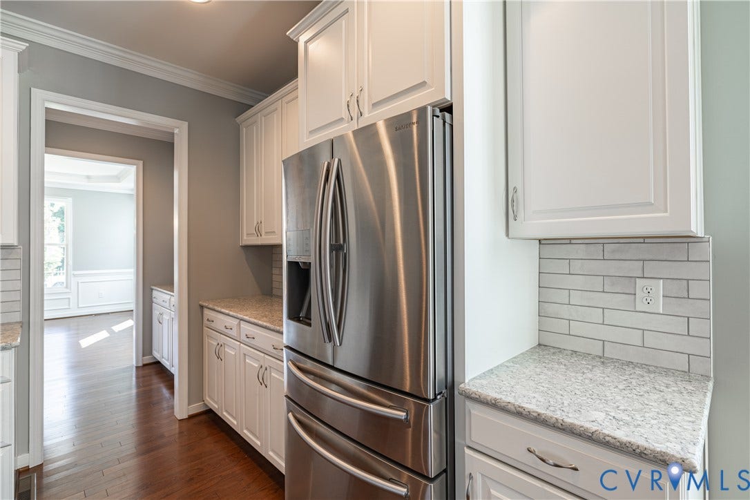 Kitchen featuring white cabinetry, light-toned countertops, a stainless steel refrigerator, and subway tile backsplash