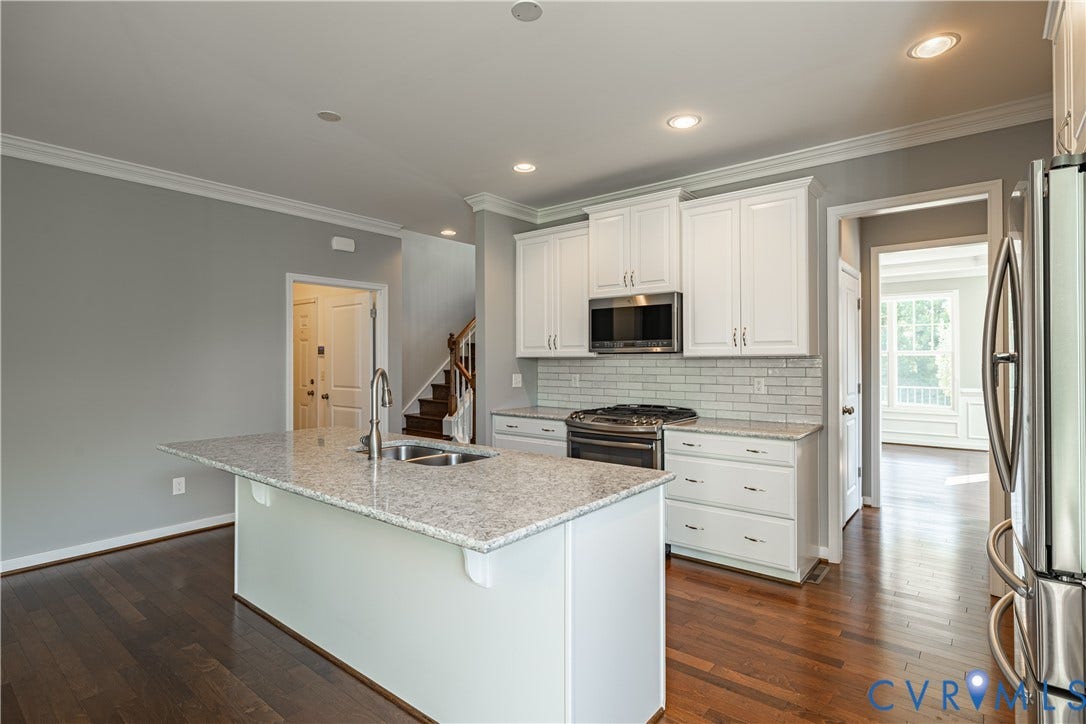 Kitchen featuring an island with a dual-basin sink, stainless steel appliances, white cabinetry, granite countertops, and a subway tile backsplash