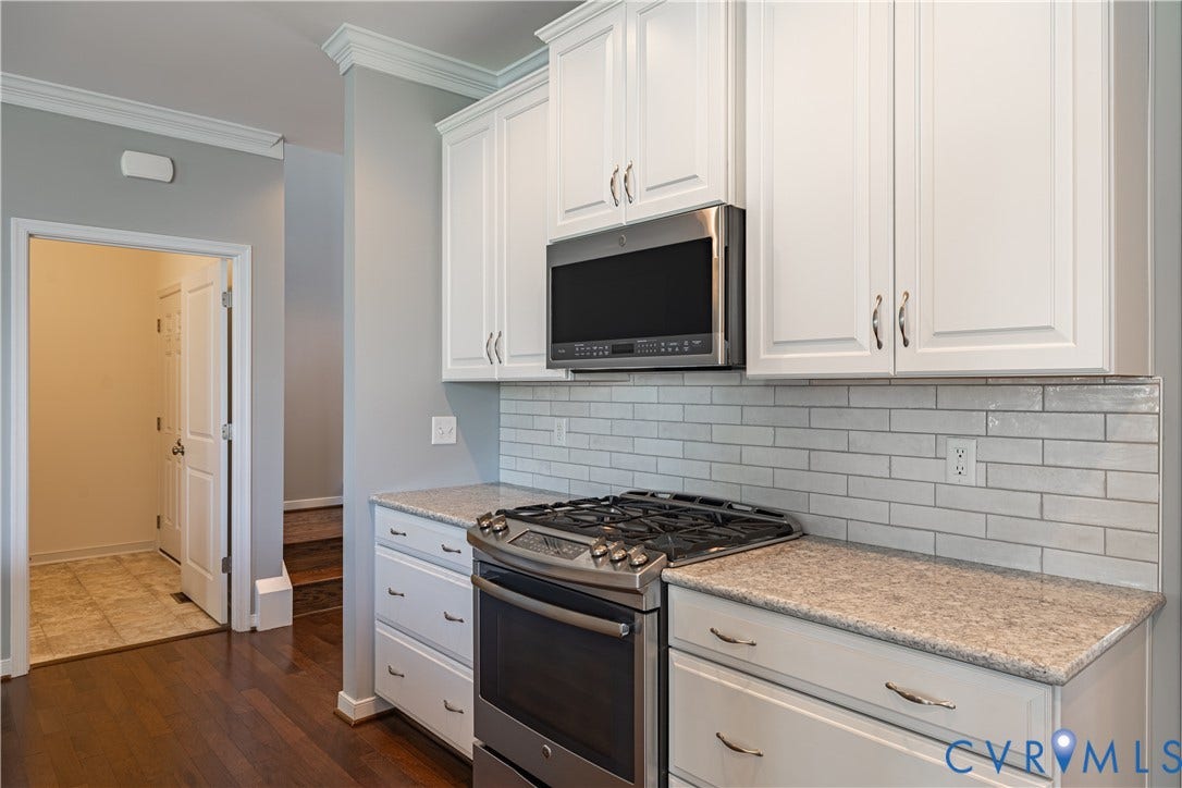 White cabinetry , stainless steel microwave, light-toned subway tile backsplash, granite countertop, and a stainless steel gas range