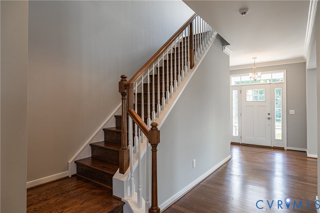 Hardwood flooring, wood staircase with white risers, decorative balusters, white front door with sidelights, and overhead chandelier