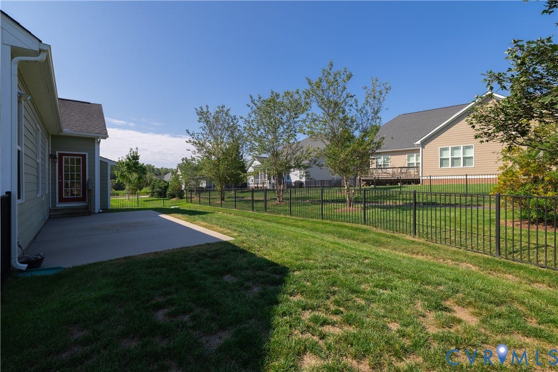 Expansive outdoor living area featuring a concrete patio, lush green lawn, and a black wrought iron fence
