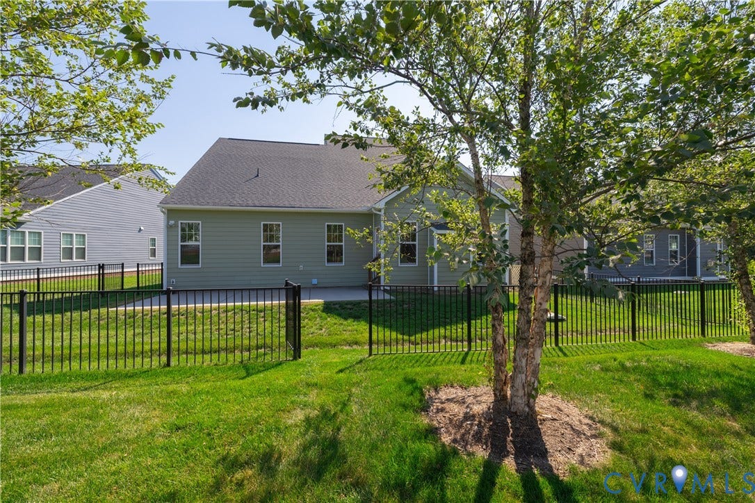 Expansive grassy yard featuring a black metal fence and mature trees