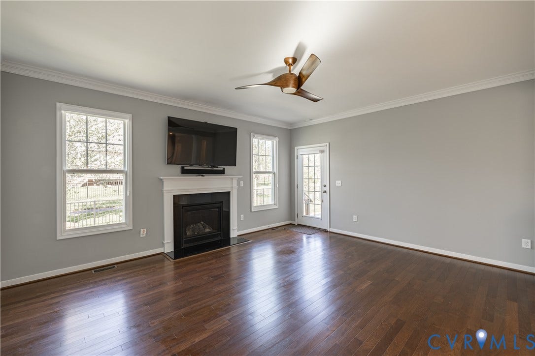 Hardwood flooring, fireplace with white mantel, ceiling fan, crown molding, and a glass-paneled exterior door