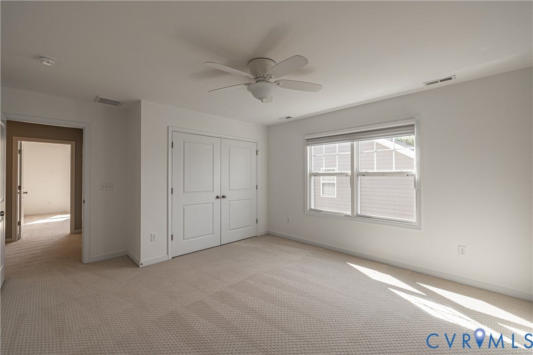Plush carpeted flooring, a ceiling fan, dual windows with blinds, and double-door storage