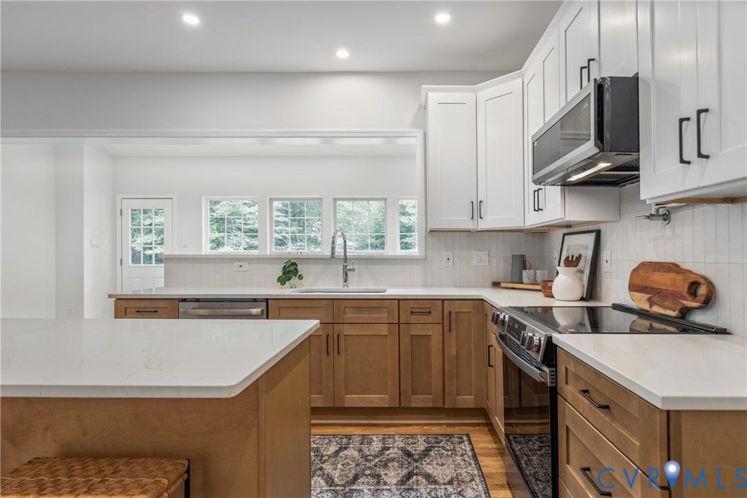 3929 Meadowview Lane, Richmond, VA 23223 Chef's kitchen featuring white shaker cabinetry paired with warm wood-finish lower cabinets, stainless steel appliances, white quartz countertops, subway tile backsplash, and a large center island with seating