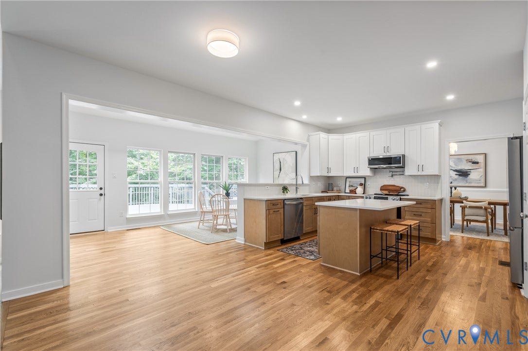 3929 Meadowview Lane, Richmond, VA 23223 Open-concept kitchen and dining area featuring white cabinetry with stainless steel appliances, a large wood-finish island with seating, wood-finish flooring throughout, and abundant natural light from multi-panel glass doors and windows overlooking the outdoor space