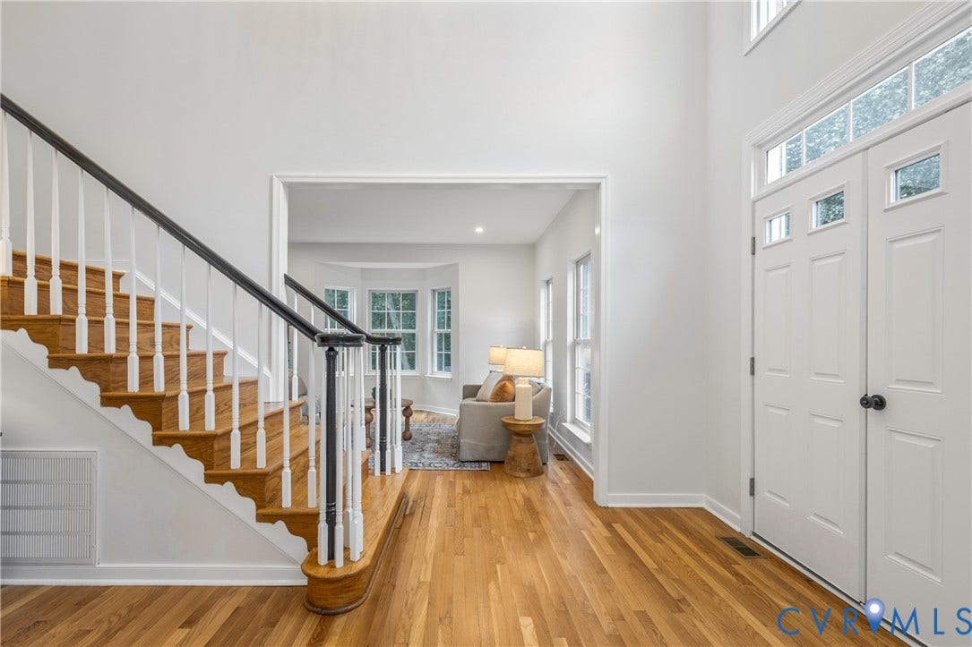 3929 Meadowview Lane, Richmond, VA 23223 Hardwood flooring throughout, a grand staircase with white spindles and dark wood handrail, transom windows above the entry doors, and a bay window in the background