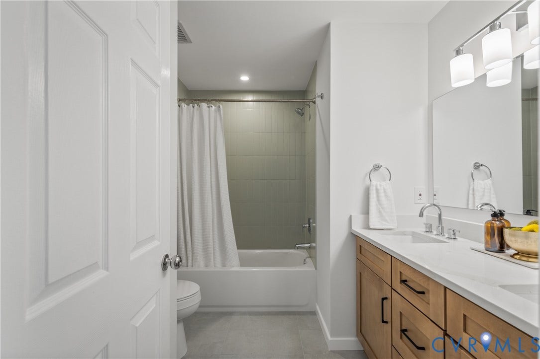 3929 Meadowview Lane, Richmond, VA 23223 Spa-inspired bathroom featuring a wood-finish vanity with dual sinks, white quartz countertop, and polished chrome faucetry