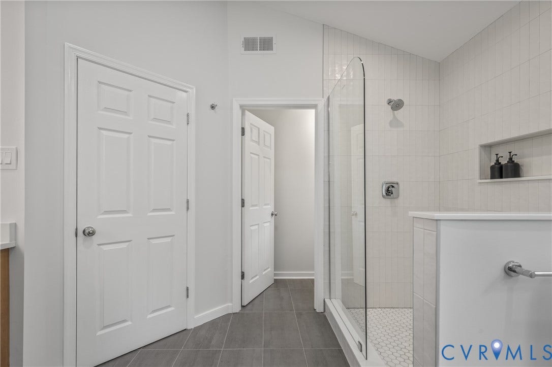 3929 Meadowview Lane, Richmond, VA 23223 Spa-inspired primary bathroom featuring a frameless glass walk-in shower enclosure with subway tile surround, dual vanity with white cabinetry and integrated storage, chrome fixtures, heated towel rack, recessed shelving, and dark tile flooring that contrasts with crisp white walls and ceiling
