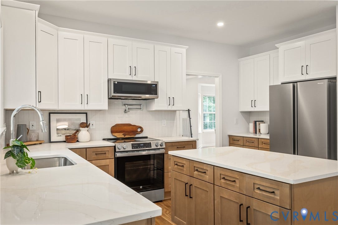 3929 Meadowview Lane, Richmond, VA 23223 Chef's kitchen featuring white shaker-style cabinetry, wood-finish island with multiple drawers and black hardware, quartz countertops, stainless steel appliances including a built-in microwave and gas range, and a modern stainless steel refrigerator