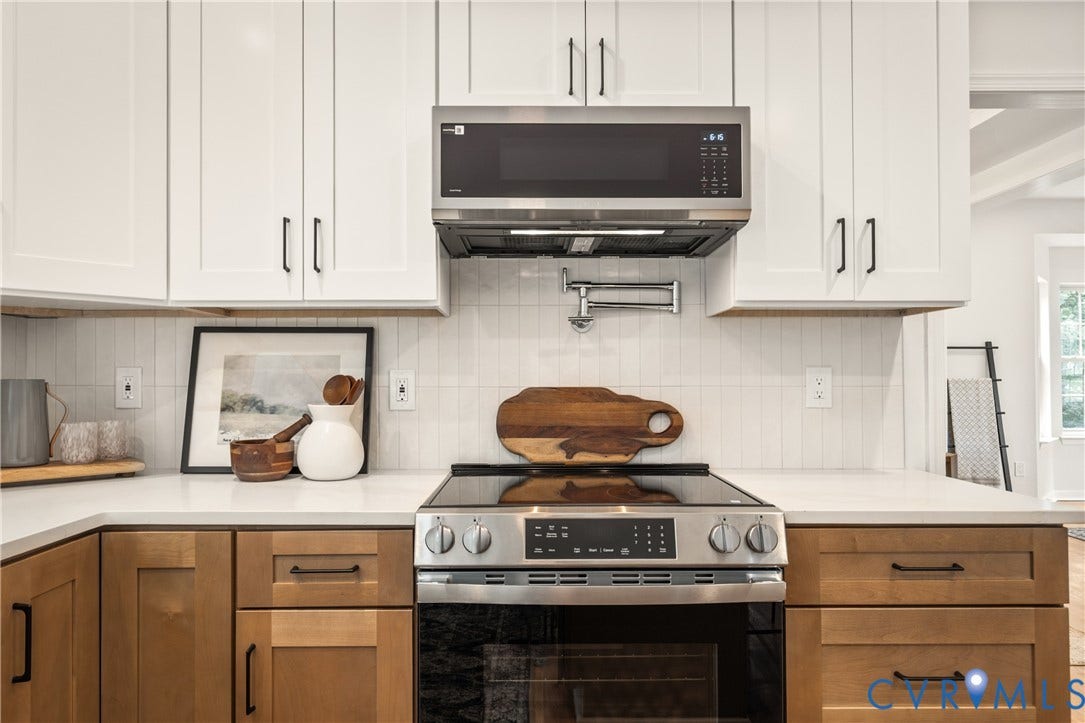 3929 Meadowview Lane, Richmond, VA 23223 White shaker-style upper cabinetry, wood-finish lower cabinetry, solid surface countertops, stainless steel electric range, and a wall-mounted pot filler