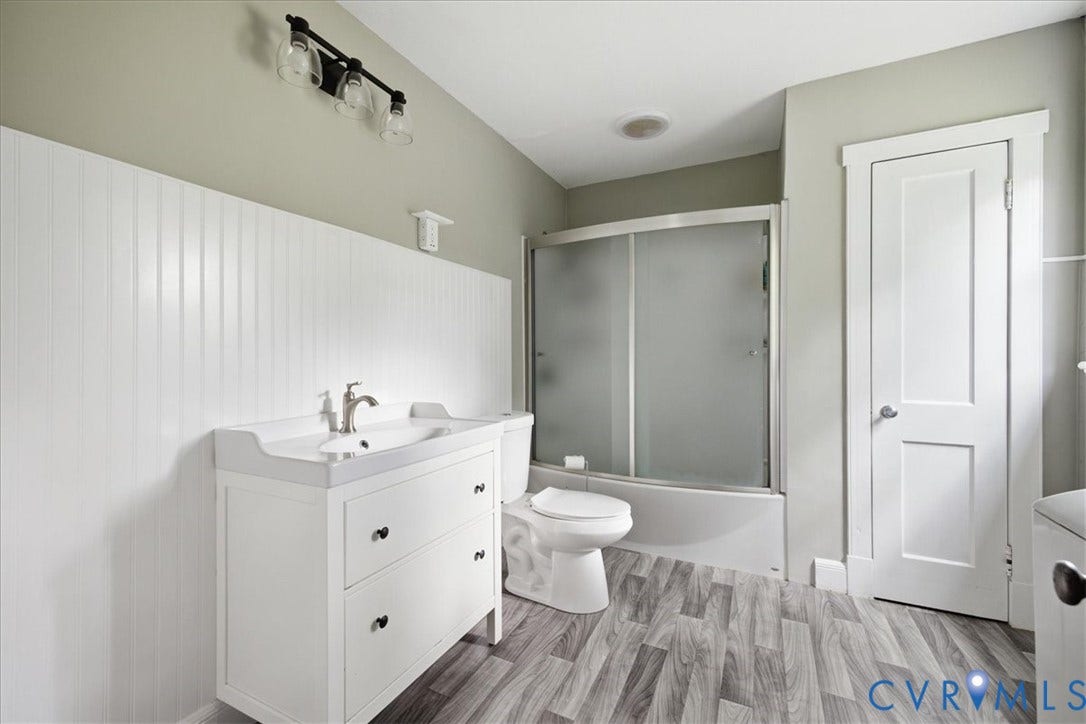 7232 Hopkins Road, North Chesterfield, VA 23237 Bathroom featuring a white vanity with integrated sink, wood-finish flooring, a shower-tub combination with sliding frosted glass doors, and vertical paneling