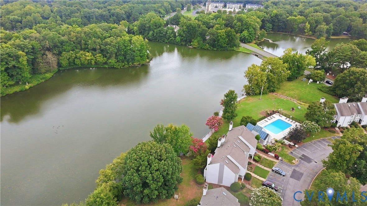 Expansive lake setting with surrounding mature trees, a structured bridge, and an outdoor swimming pool with an enclosed area