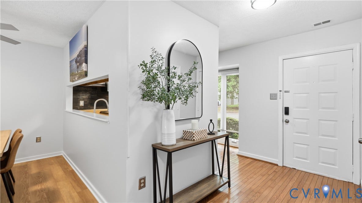 Wood-finish flooring throughout, white paneled entry door, pass-through opening to kitchen, and recessed lighting