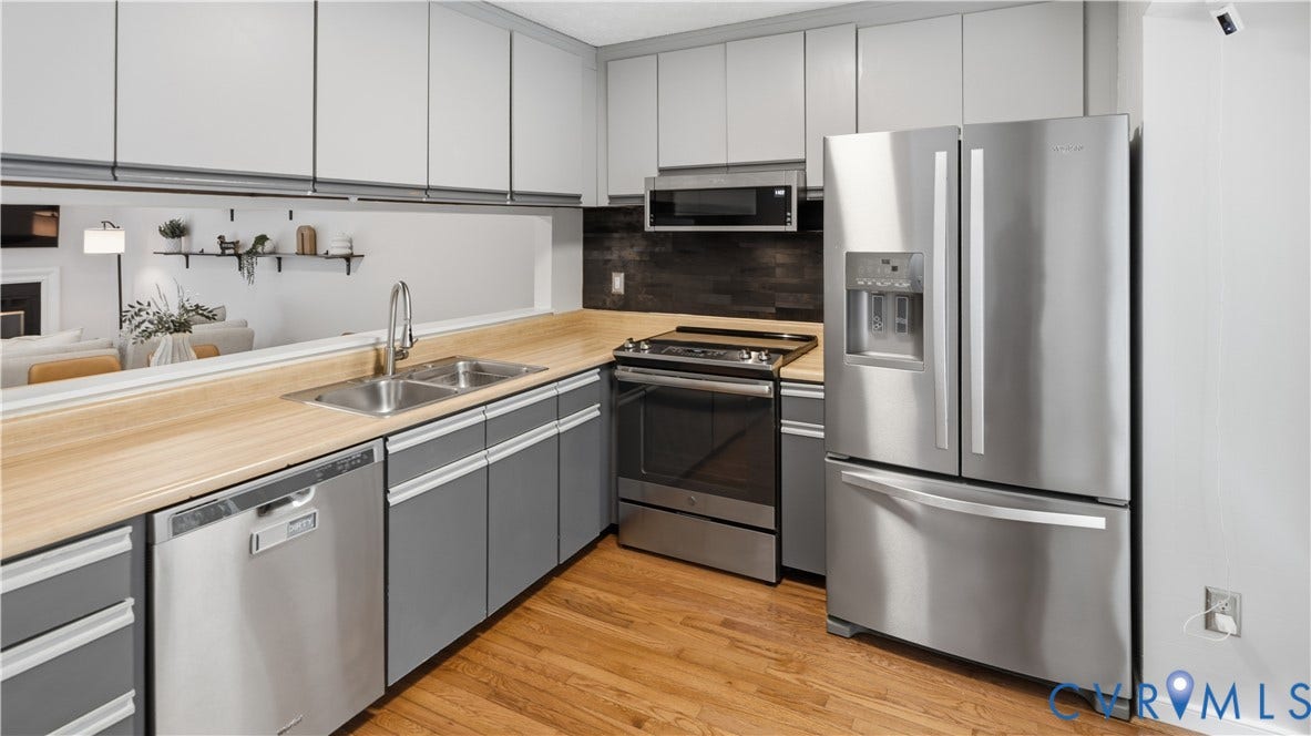 Kitchen featuring stainless steel appliances, wood-finish countertops, dual-basin sink, and overhead cabinetry
