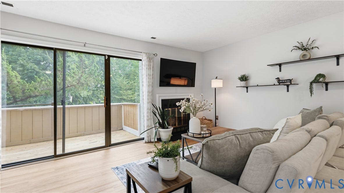 Living area featuring light wood-finish flooring, a fireplace with a white mantel, and a wall with two built-in floating shelves