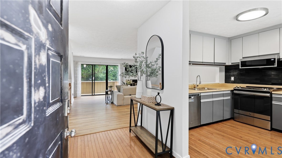 Hardwood flooring throughout, modern kitchen appliances, light-toned upper cabinetry, black subway tile backsplash, and a sliding glass door to an outdoor space