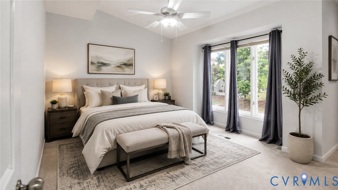 Vaulted ceiling with ceiling fan, expansive bay window, plush carpeting, upholstered headboard, and two wood-finish nightstands