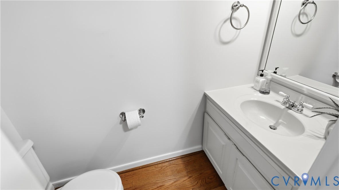Vanity with integrated sink, chrome faucet, wall-mounted mirror, and wood-finish flooring