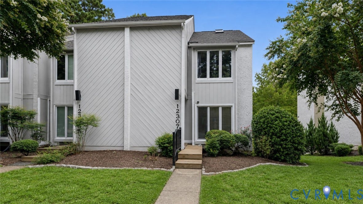 Two-story facade with multiple windows, concrete walkway, and landscaped garden beds