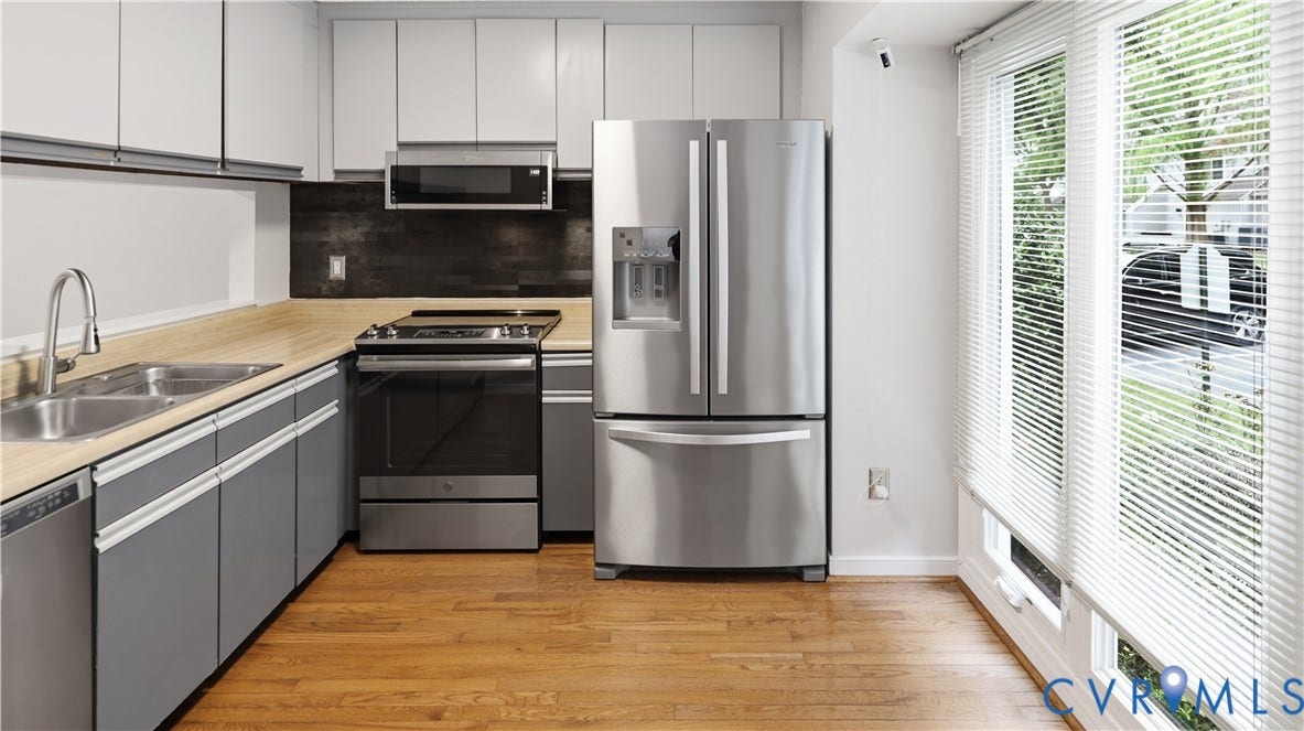 Kitchen featuring stainless steel appliances, light wood-finish countertops, grey lower cabinetry, white upper cabinetry, and wood-finish flooring