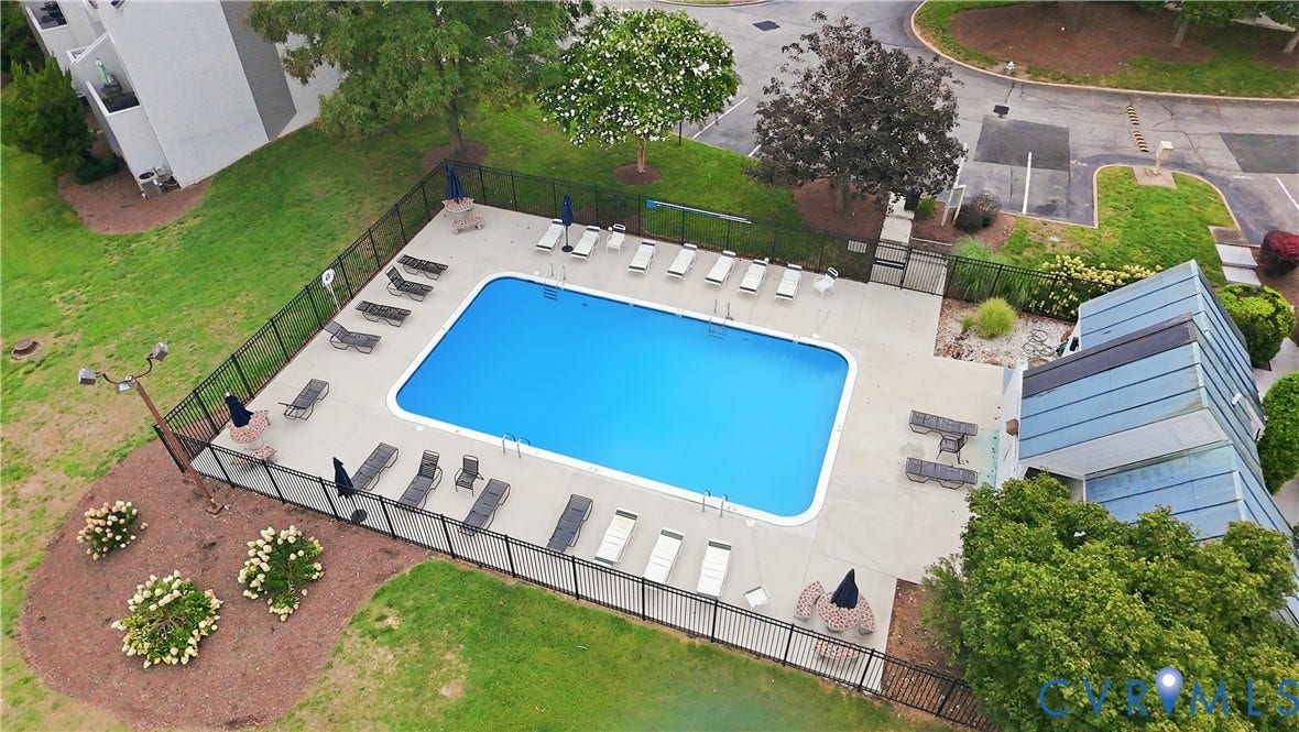 Outdoor swimming pool with a surrounding paved deck, secured by a perimeter fence