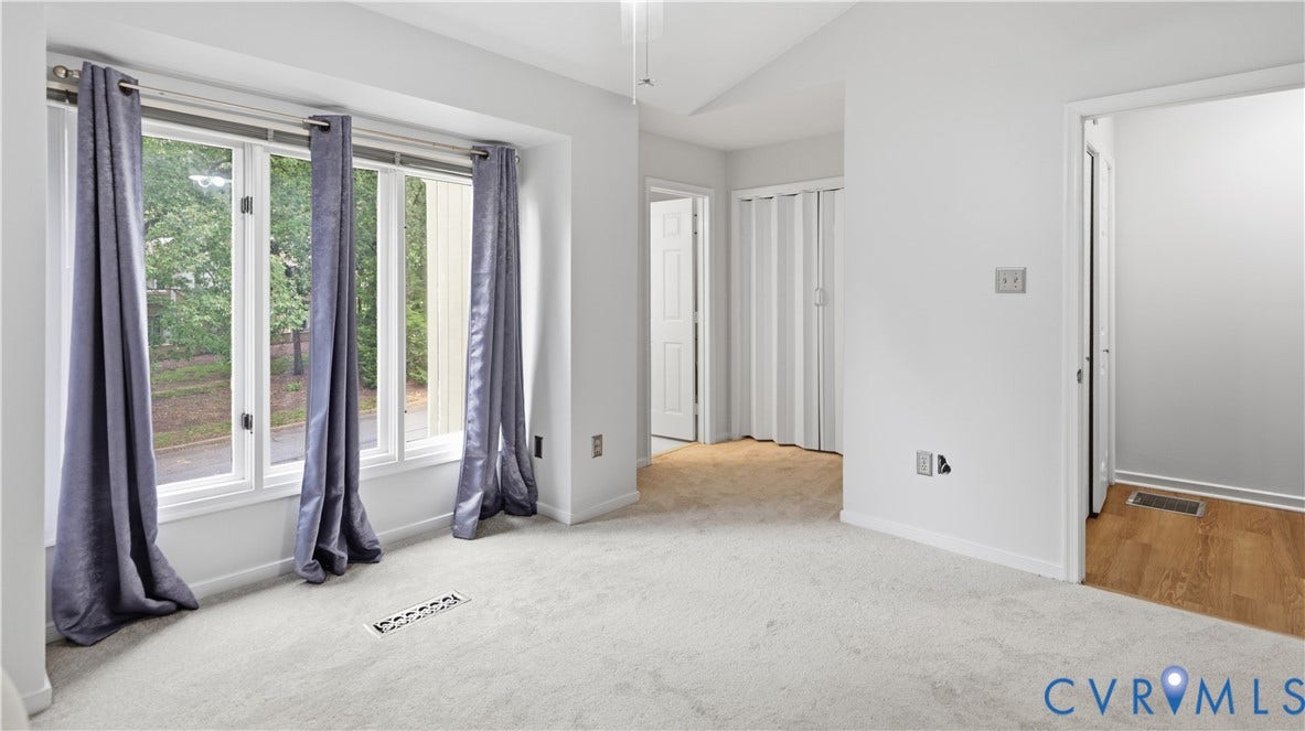 Bay window with multiple panes, light-colored carpeting, white interior walls, and a ceiling fan