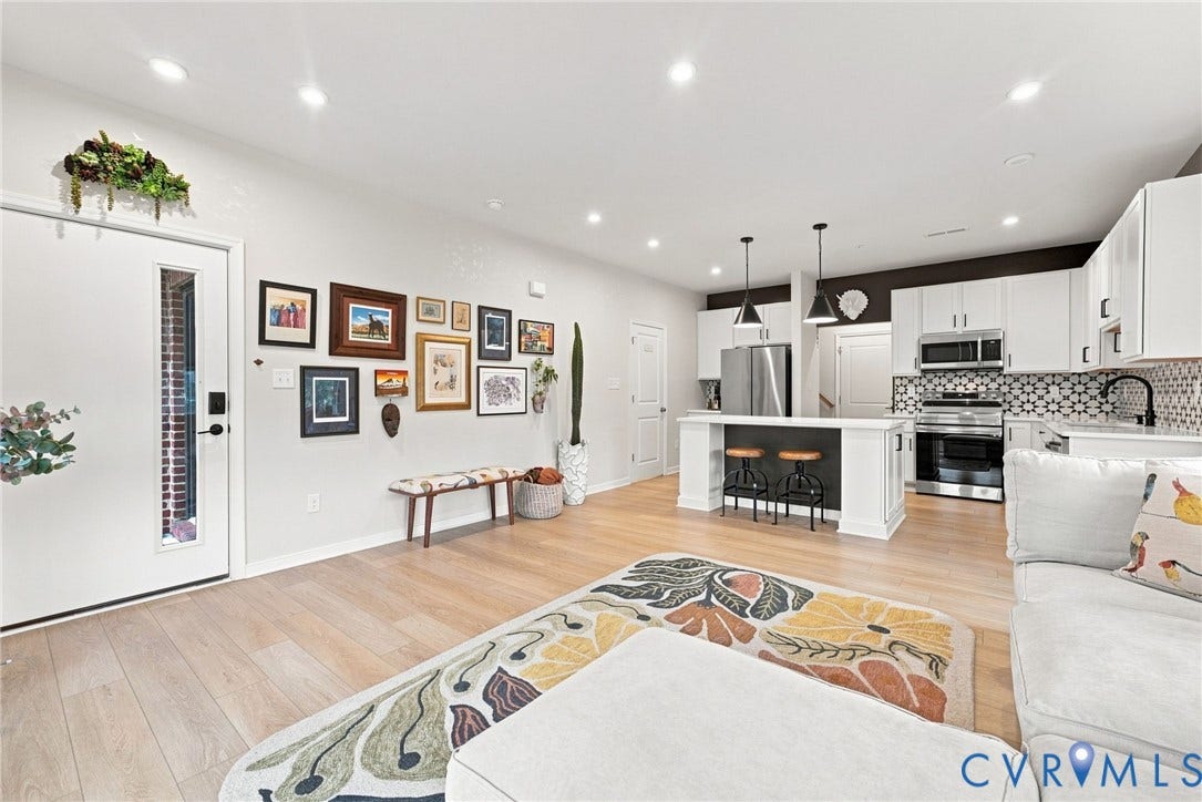 2445 Ownby Lane, #B15, Greater Scott's Addition, Richmond, VA 23220 Bright open-concept living space with light wood-finish flooring, recessed lighting, and a kitchen featuring stainless steel appliances, white cabinetry, and a geometric tile backsplash