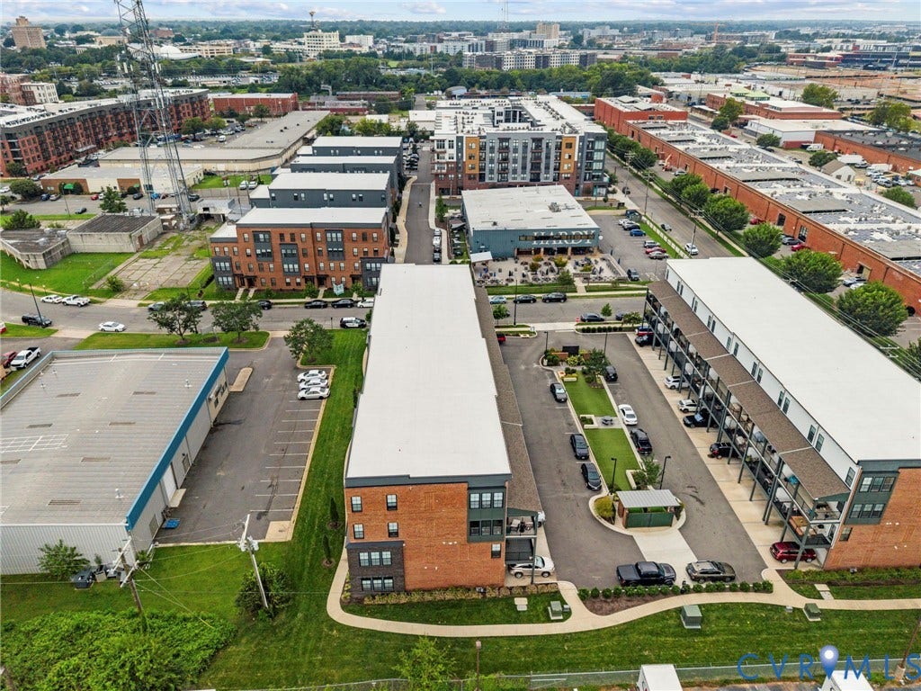 2445 Ownby Lane, #B15, Greater Scott's Addition, Richmond, VA 23220 Aerial perspective of a mixed-use development featuring multi-story residential buildings, commercial structures, and surface parking areas